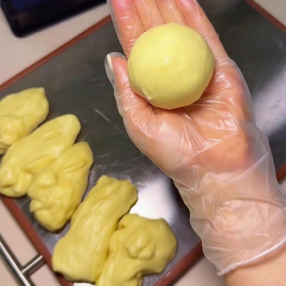 A close-up of a hand holding a smooth dough ball and dipping it into a bowl filled with white sesame seeds.