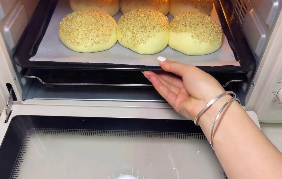 A tray of proofed, sesame-topped dough balls being slid into a preheated oven.