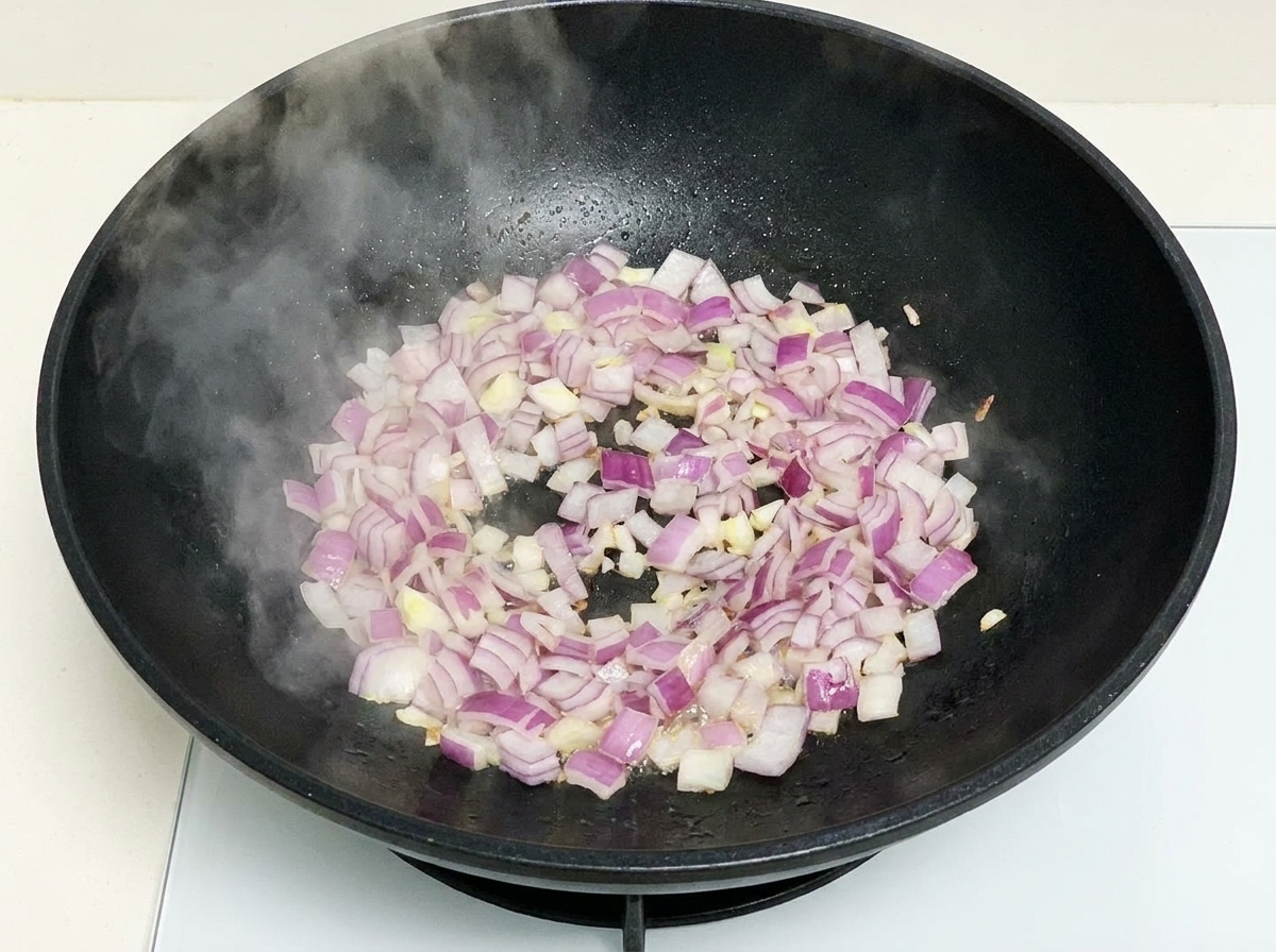 Chopped purple onions sautéing in a hot black wok with visible steam rising.