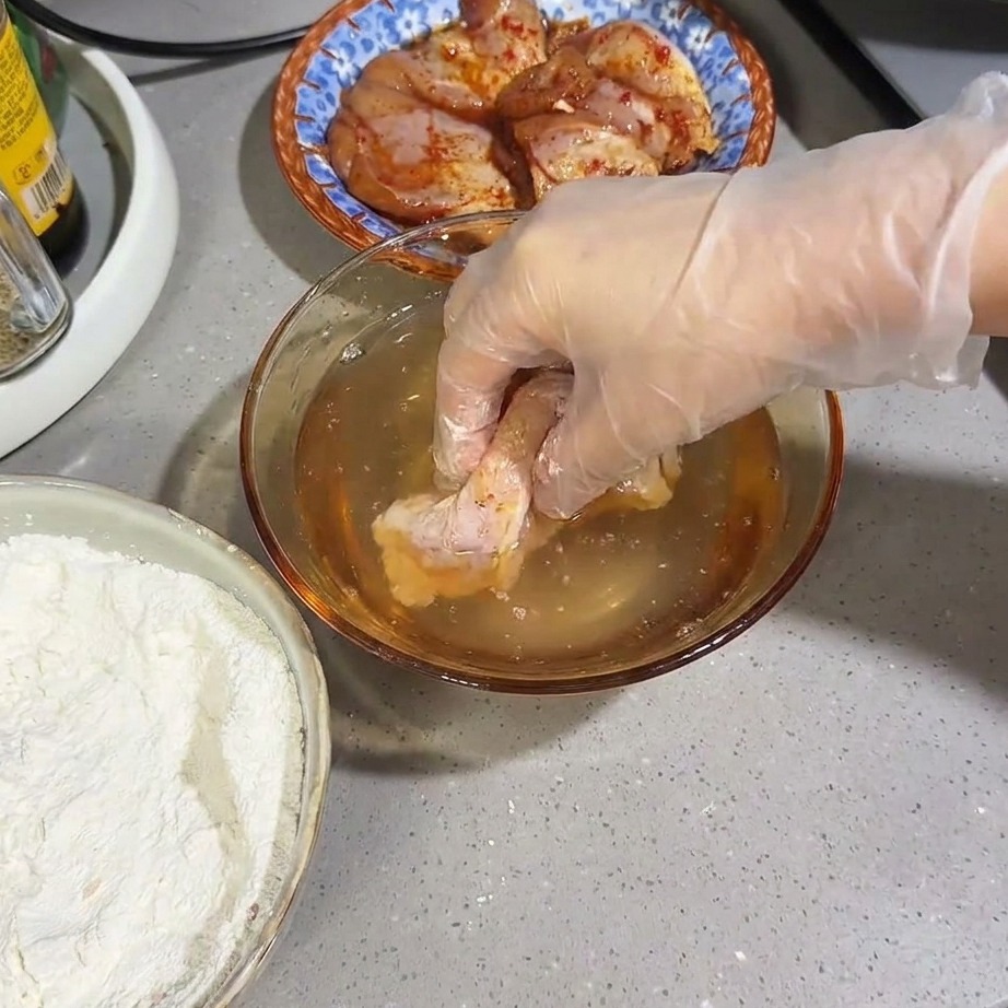 A flour-coated raw chicken thigh being submerged briefly in a bowl of water.