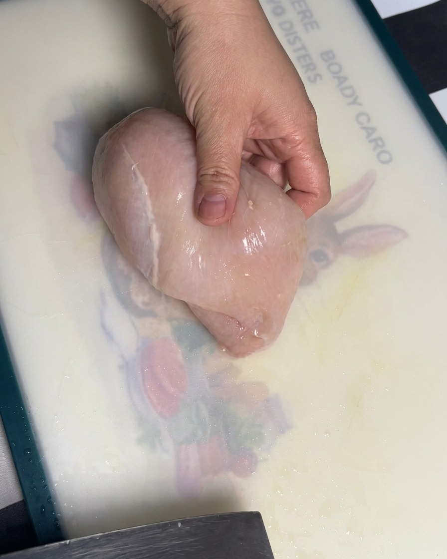 Raw chicken breast being sliced into even pieces on a cutting board.