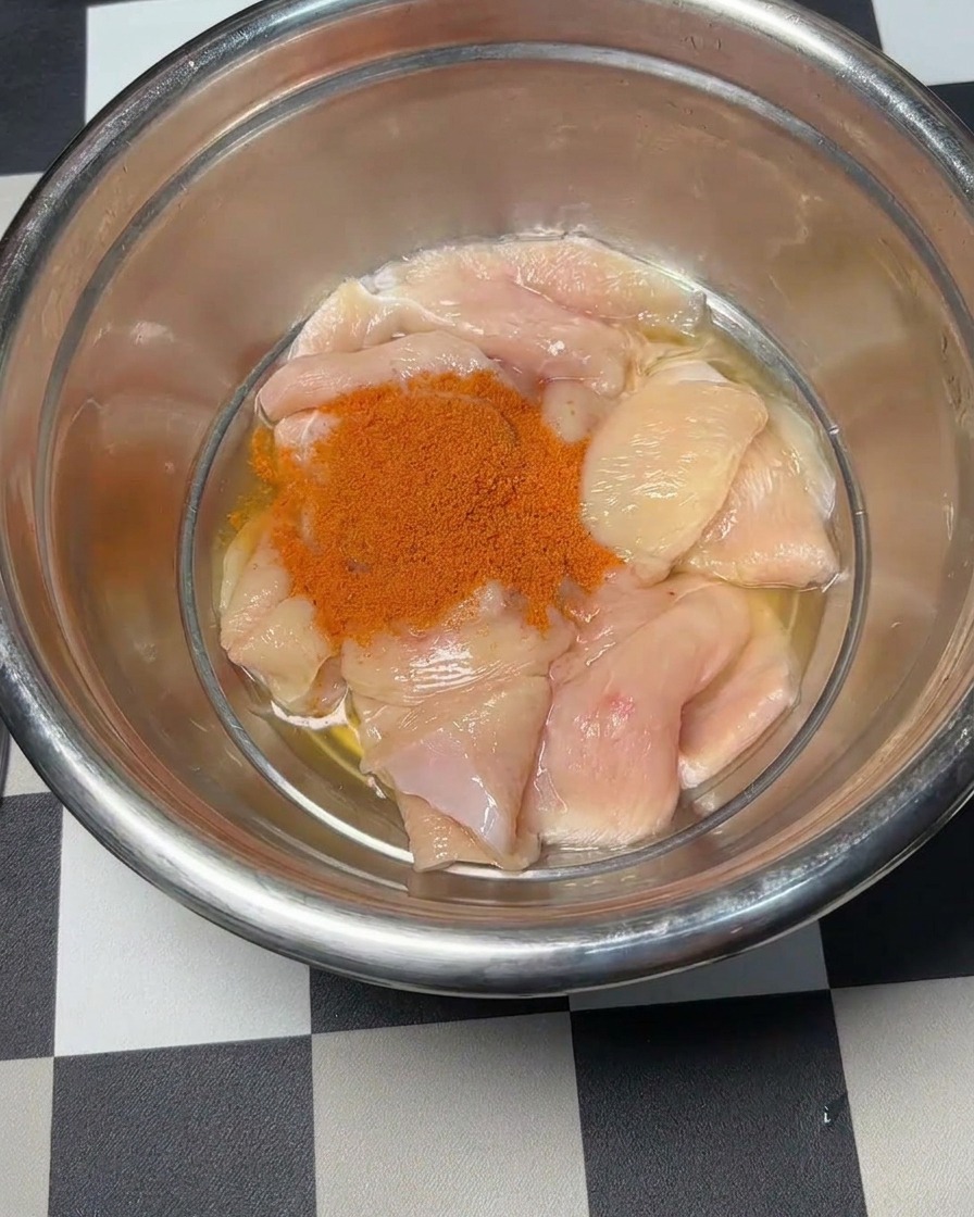 Red Orleans marinade powder being poured over raw chicken pieces.