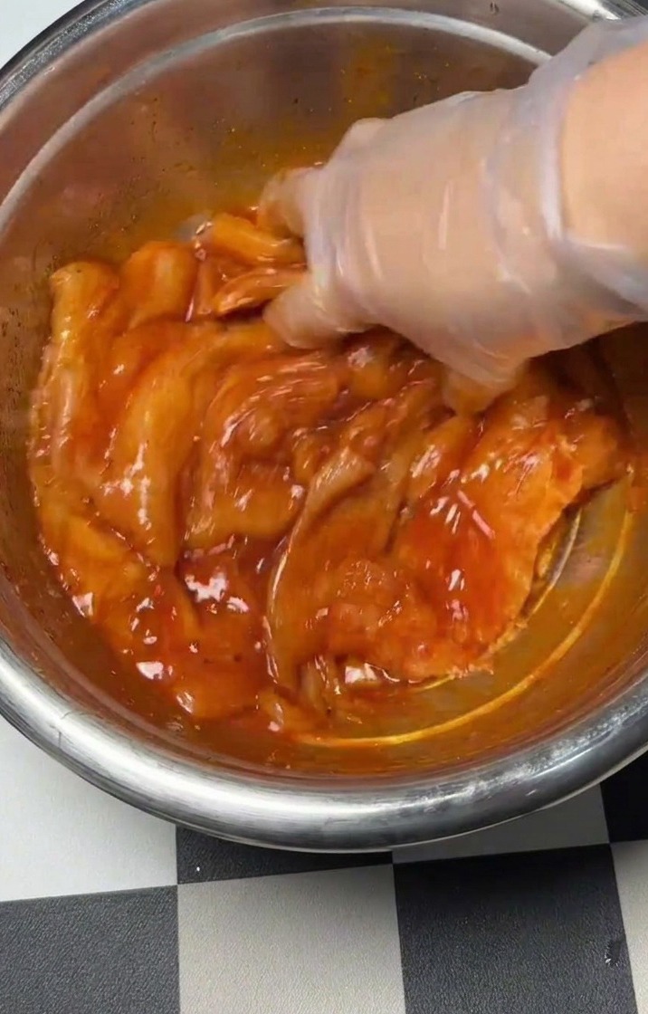 Hand mixing the seasoned chicken and marinade in a metal bowl.