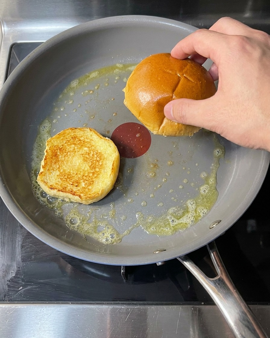 Burger buns resting in a pan with bubbling melted butter, undergoing the toasting process.