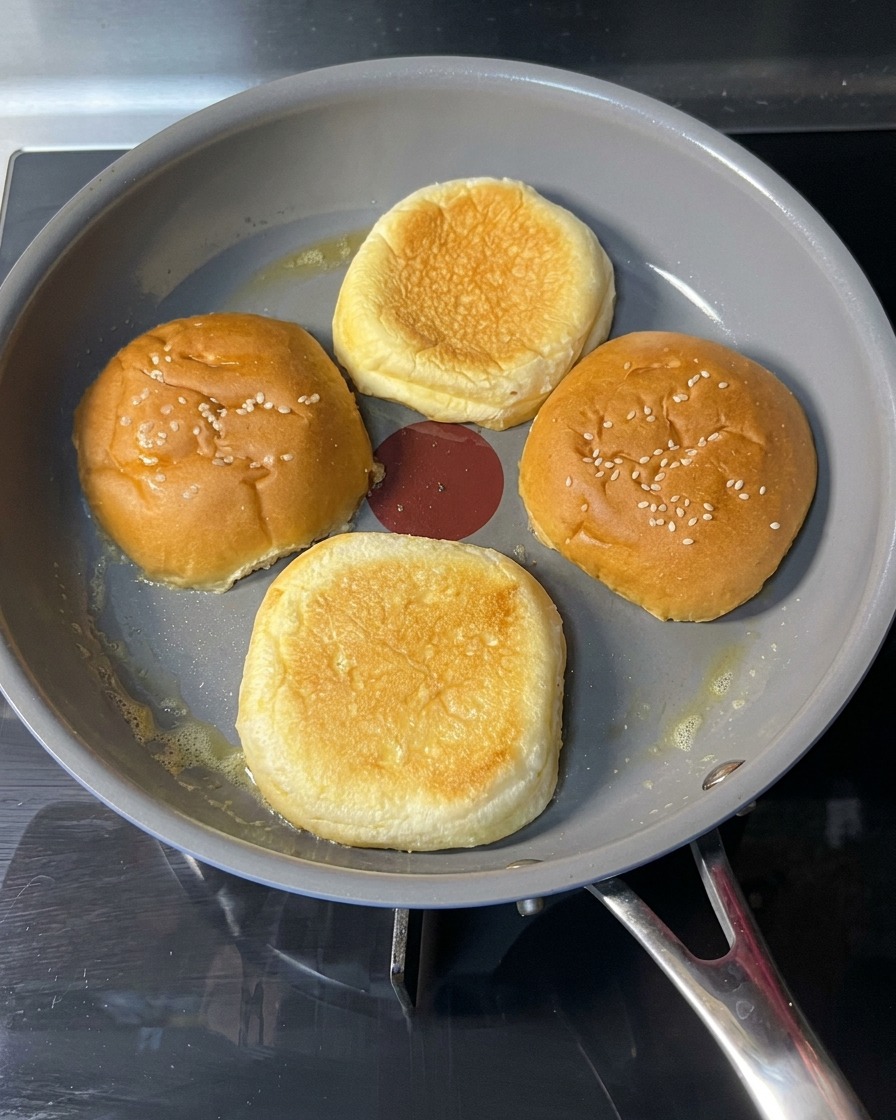 A hand flipping a toasted burger bun in a pan to show a perfectly browned and crisp golden surface.
