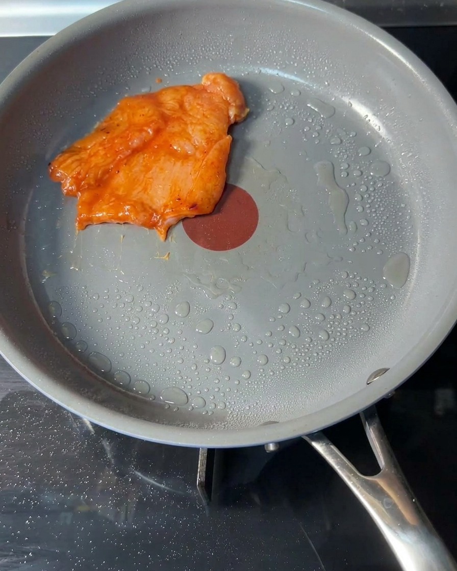 Raw seasoned chicken patties placed into a hot pan with a light coating of cooking oil.