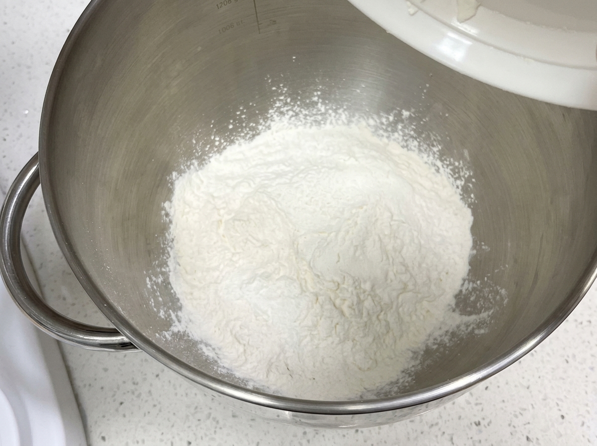 Dry flour and ingredients sitting in a clean metal stand mixer bowl.