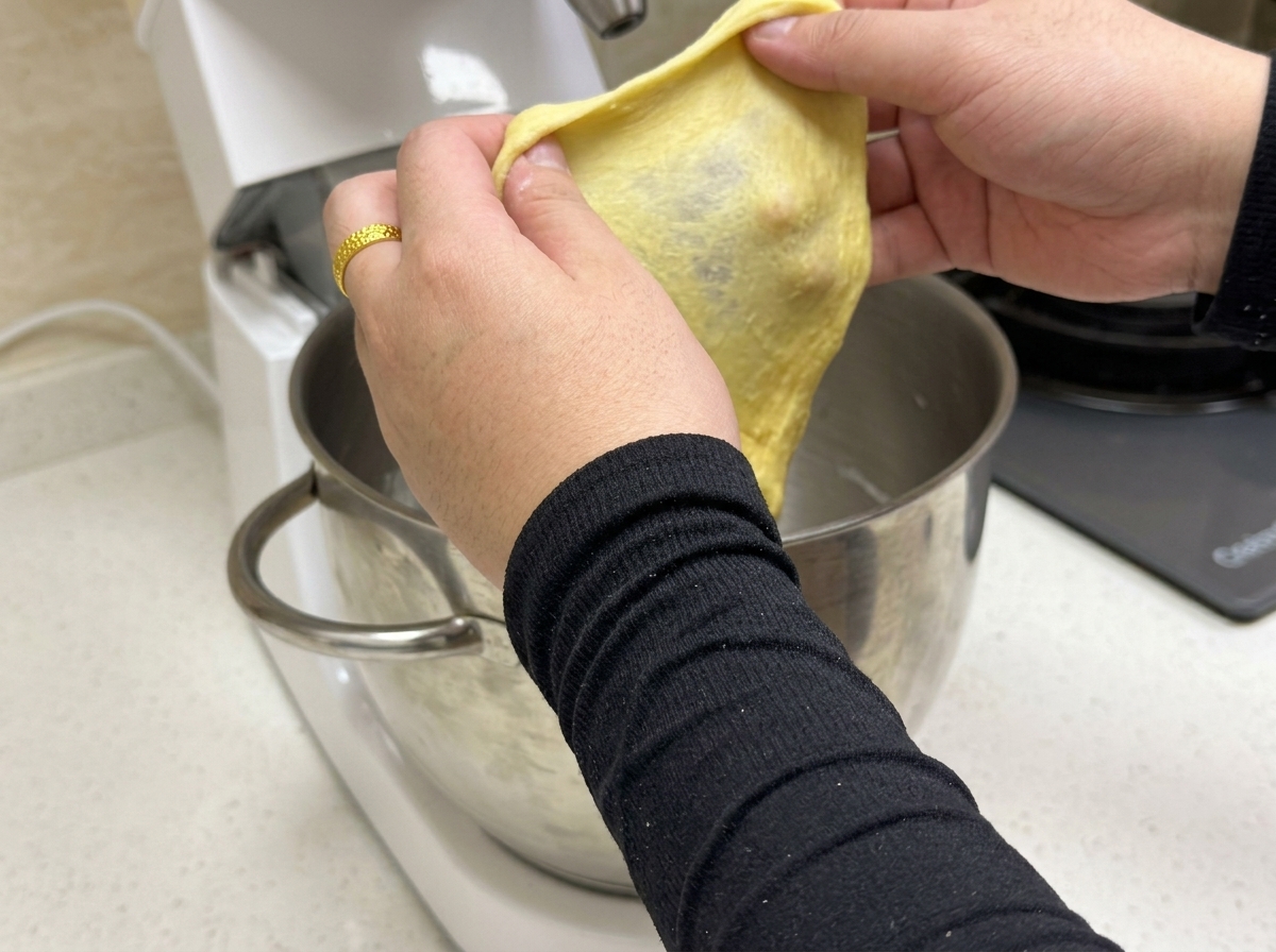 A small portion of yellow dough being stretched to show a thin, elastic gluten membrane.
