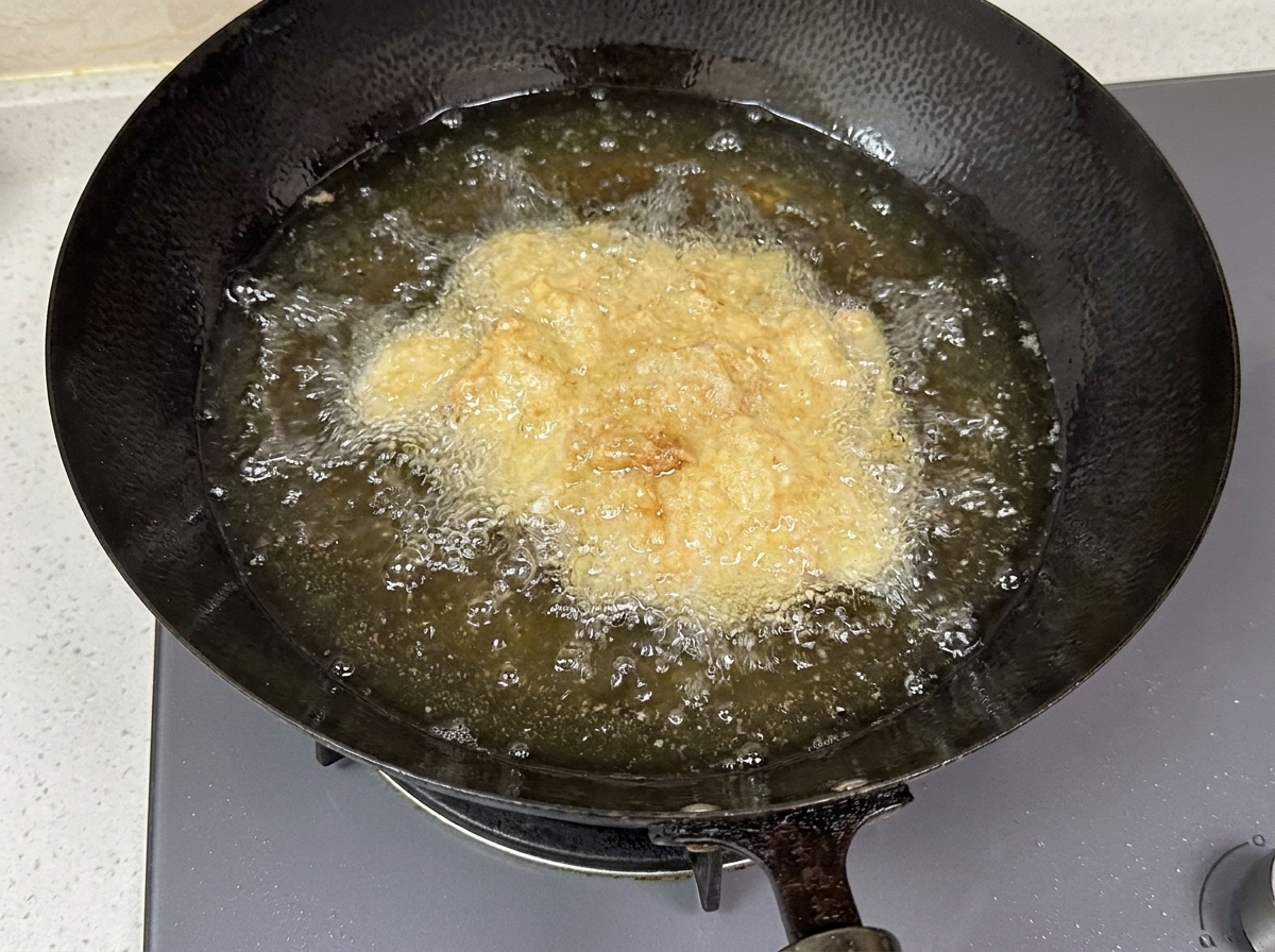 Breaded chicken pieces bubbling in hot oil inside a dark wok.