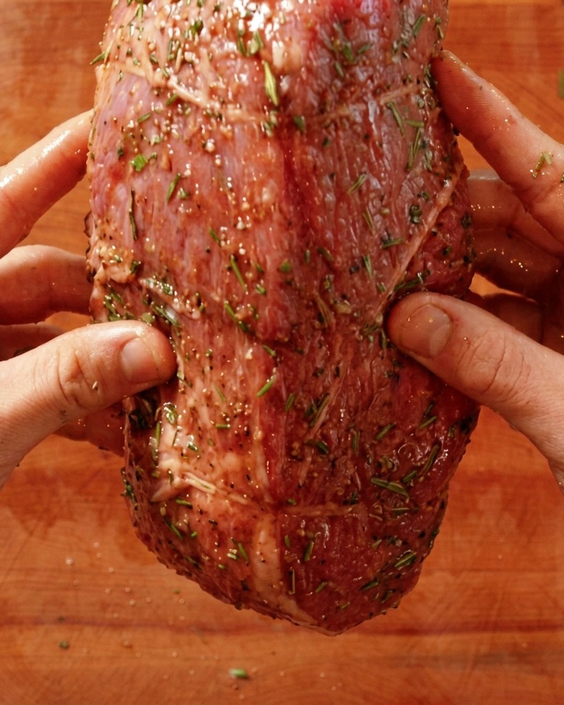 Hands placing a seasoned raw beef roast into a hot searing pan.