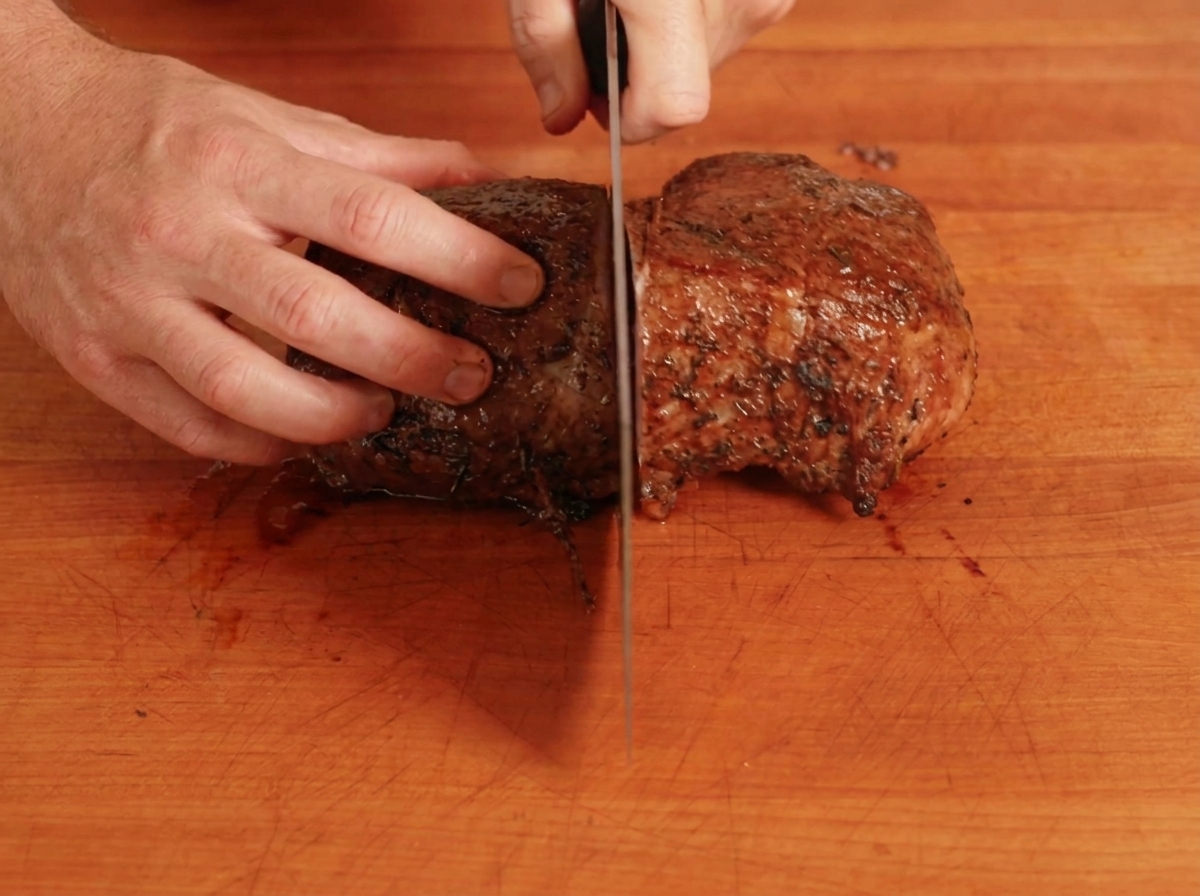 A cooked beef roast being sliced in half on a wooden cutting board.