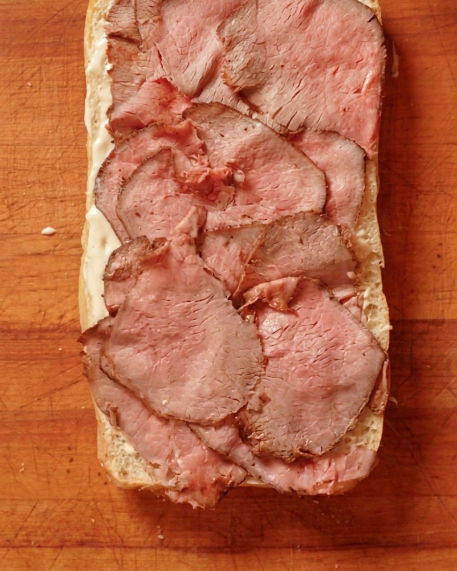 Thinly sliced cooked roast beef arranged over a layer of spread on a piece of bread.