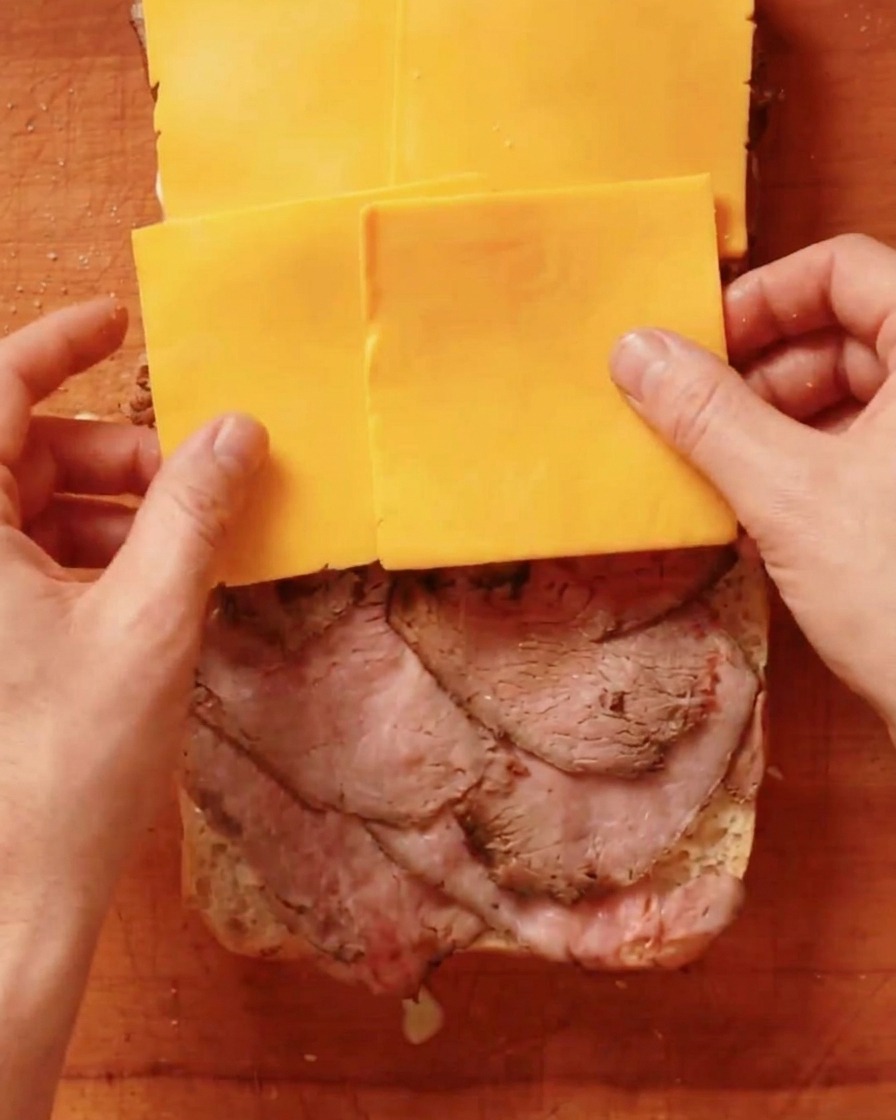 Slices of yellow cheddar cheese being placed on top of a layer of roast beef.