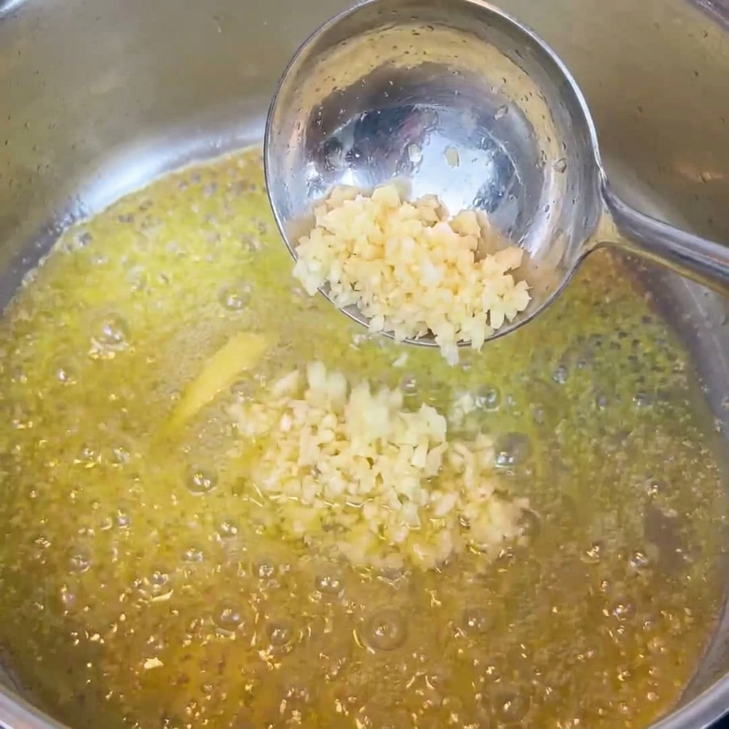 Minced garlic being stirred into melted butter in a pan.