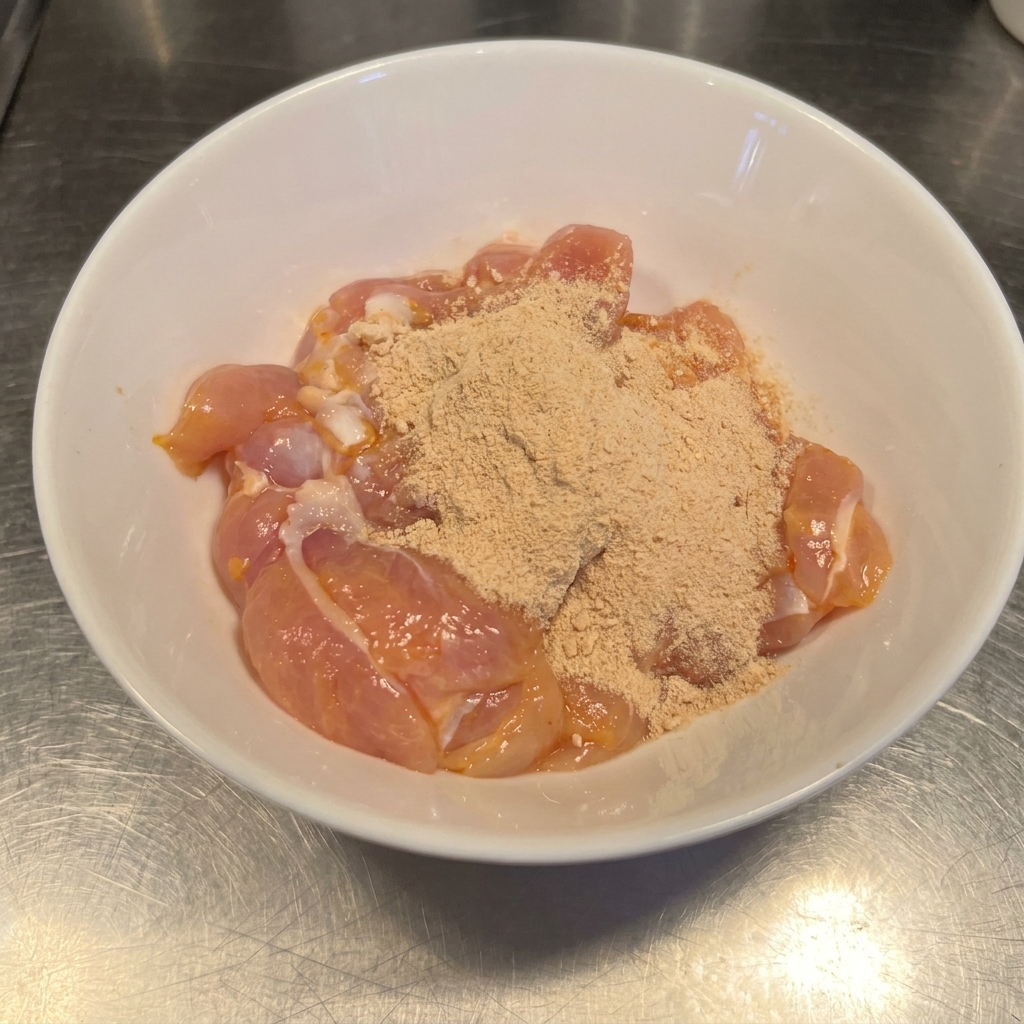 Raw chicken thighs in a bowl coated with a blend of reddish-brown chili powder and garlic seasoning.