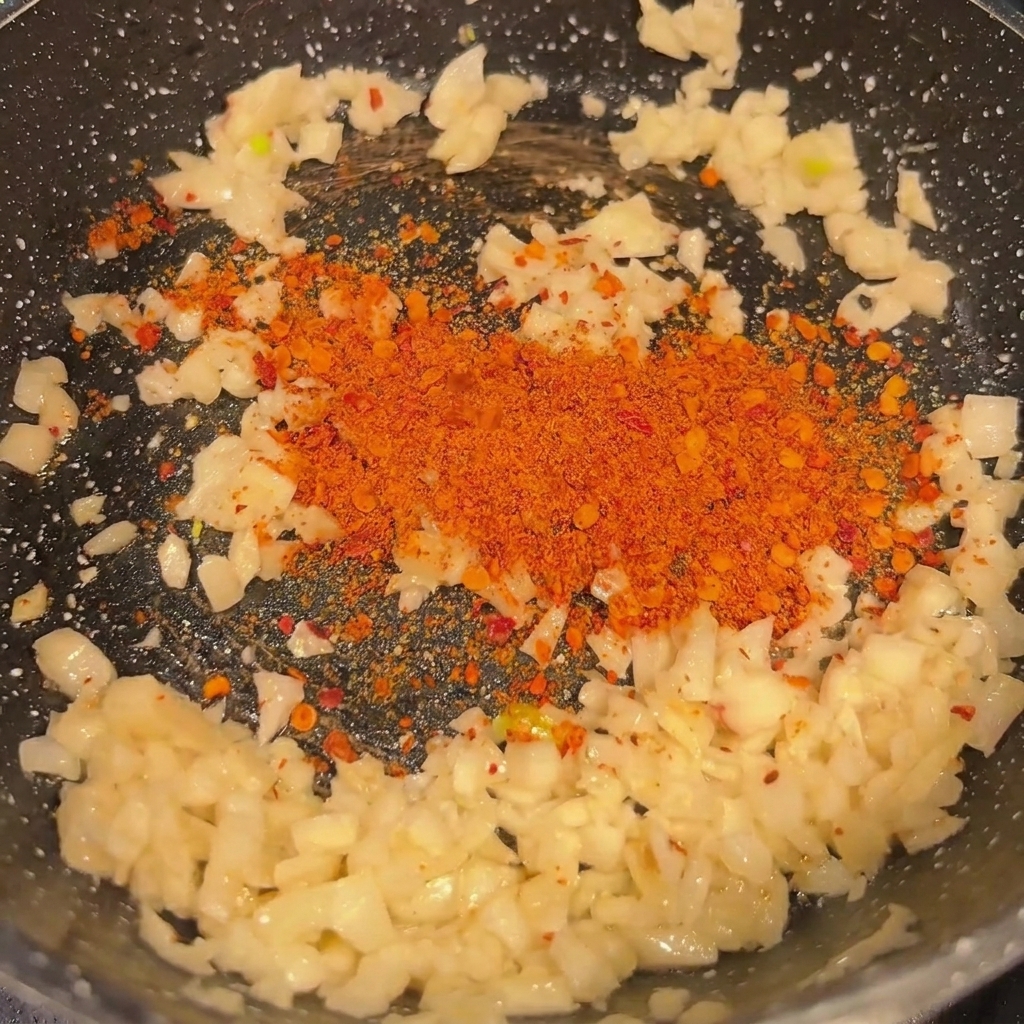 Minced garlic and chili powder being sautéed in a hot black pan until fragrant.