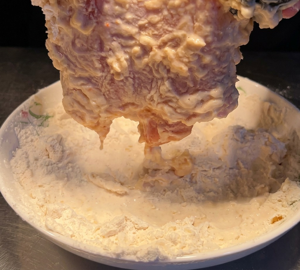 The water-dipped chicken being pressed into a plate of dry flour to build a second coating.