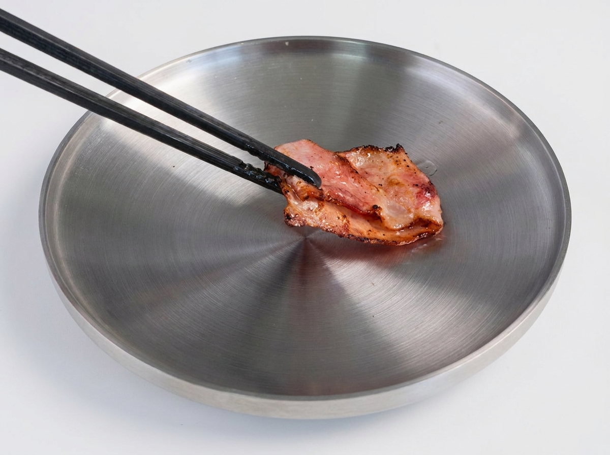 A spatula flipping a browned beef patty in a hot frying pan.