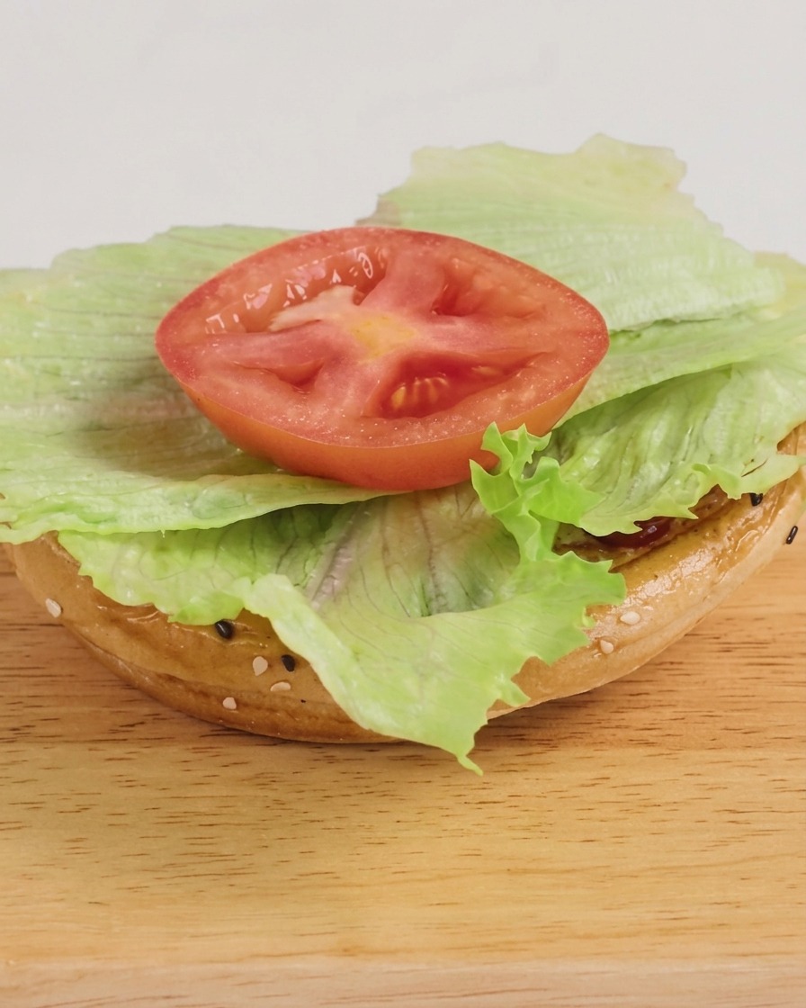 A freshly assembled burger with lettuce, a cheesy beef patty, and a drizzle of BBQ sauce, ready to be served.