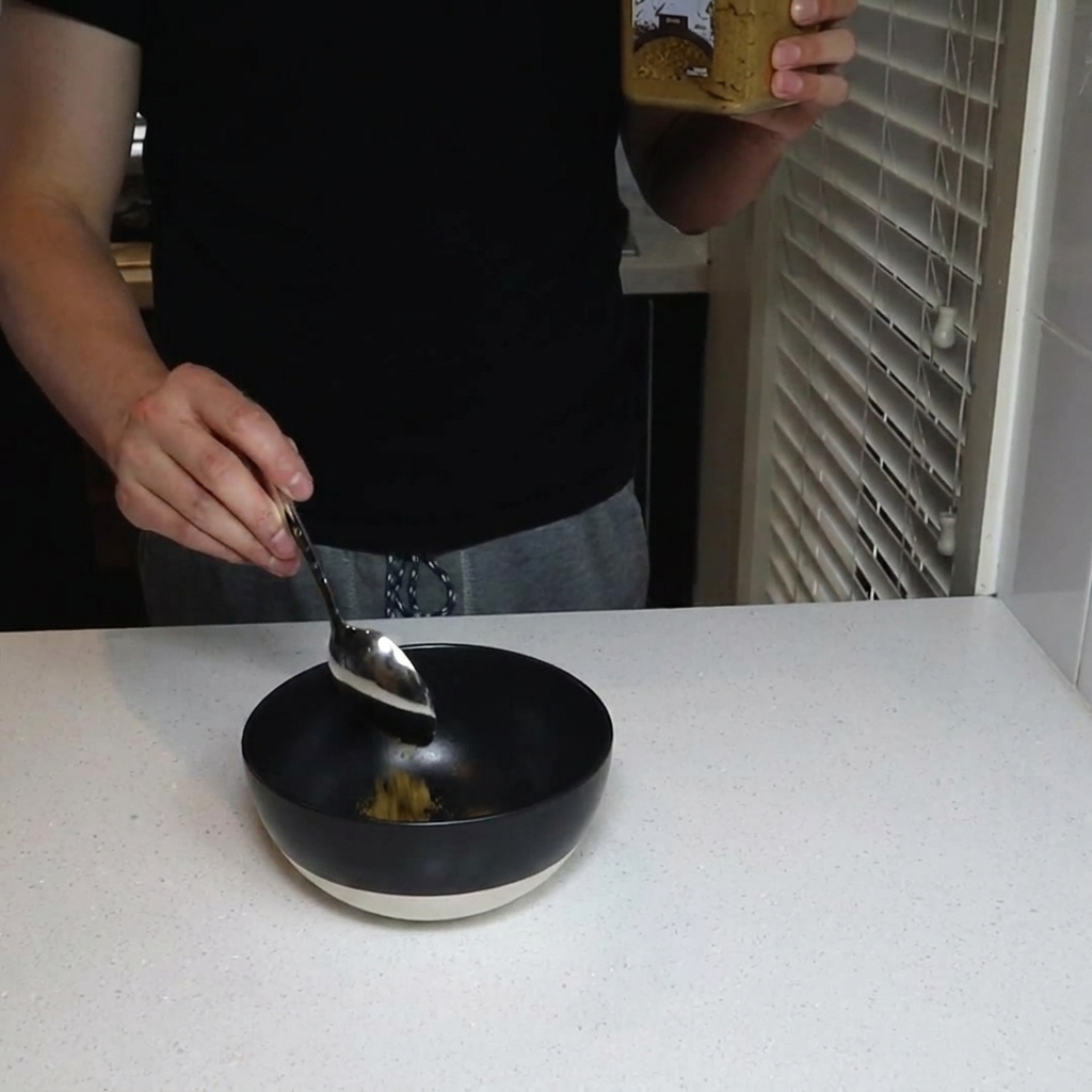 Cumin powder being poured into a black mixing bowl.