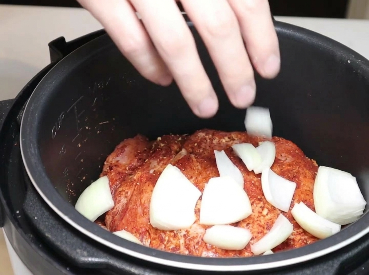 Onion wedges and dried red chilies being placed into the pressure cooker with the seasoned pork.