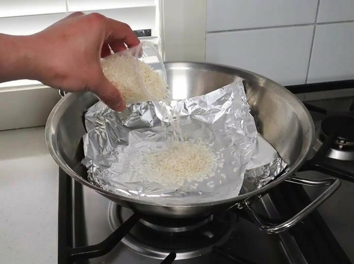 Raw rice and wood chips spread evenly on a foil-lined wok.