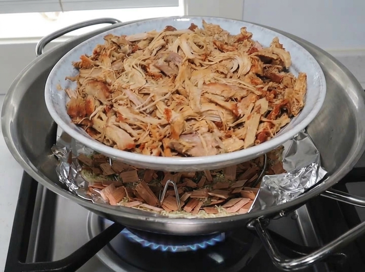A plate of shredded pork resting on a rack inside the wok over the smoking mixture.