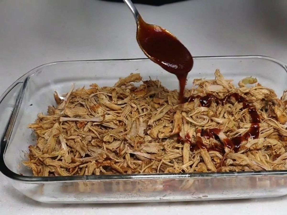 BBQ sauce being spooned over a dish of tender smoked shredded pork.