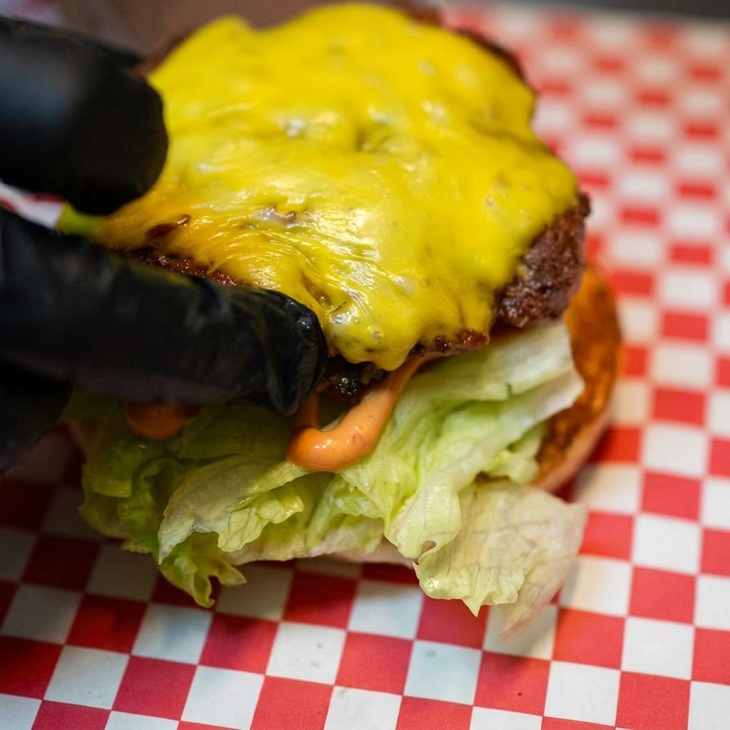 The melted cheese-covered beef patty being placed onto the lettuce and tomato base.