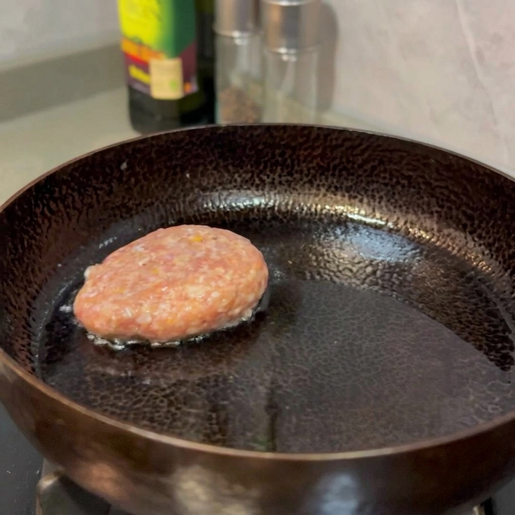 Beef patties frying in a pan until golden brown and set.