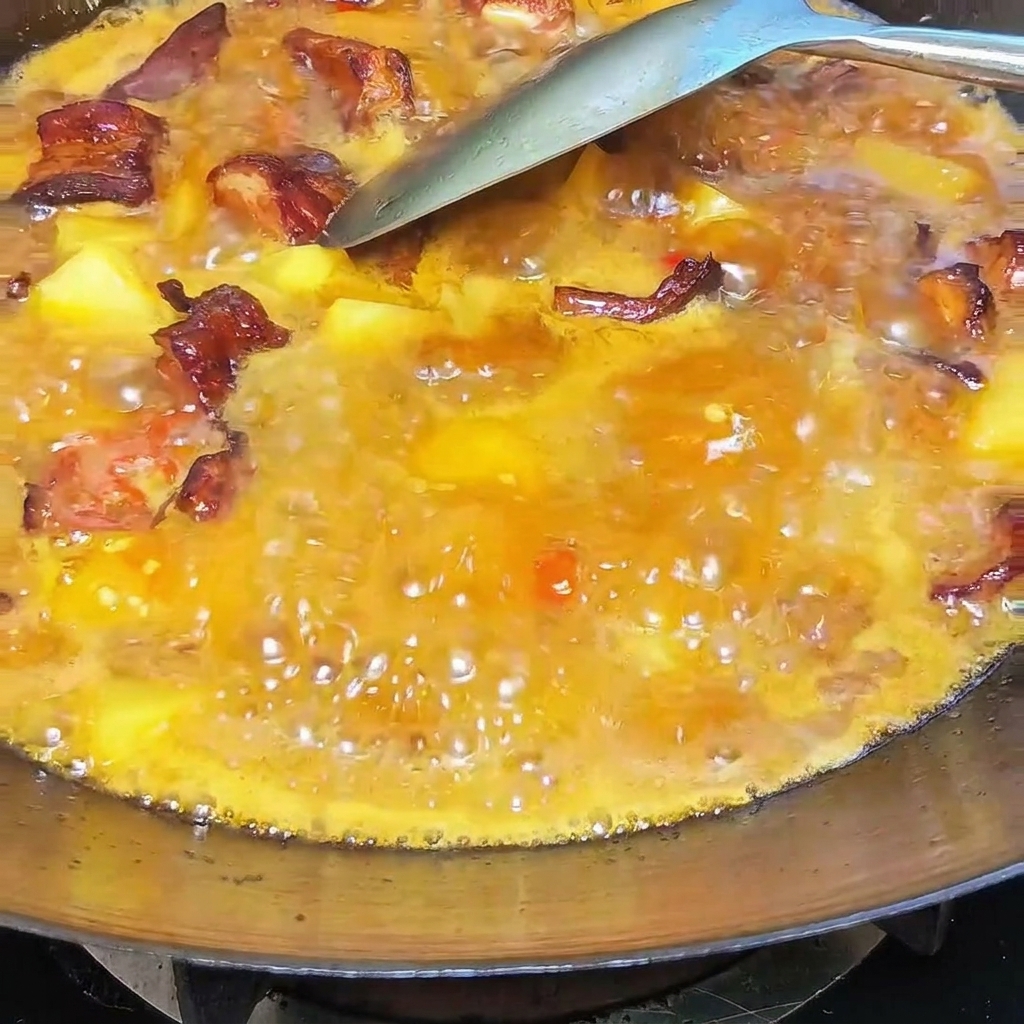 A spoonful of creamy white lard being mixed into the bubbling stew of ribs and potatoes in a wok.