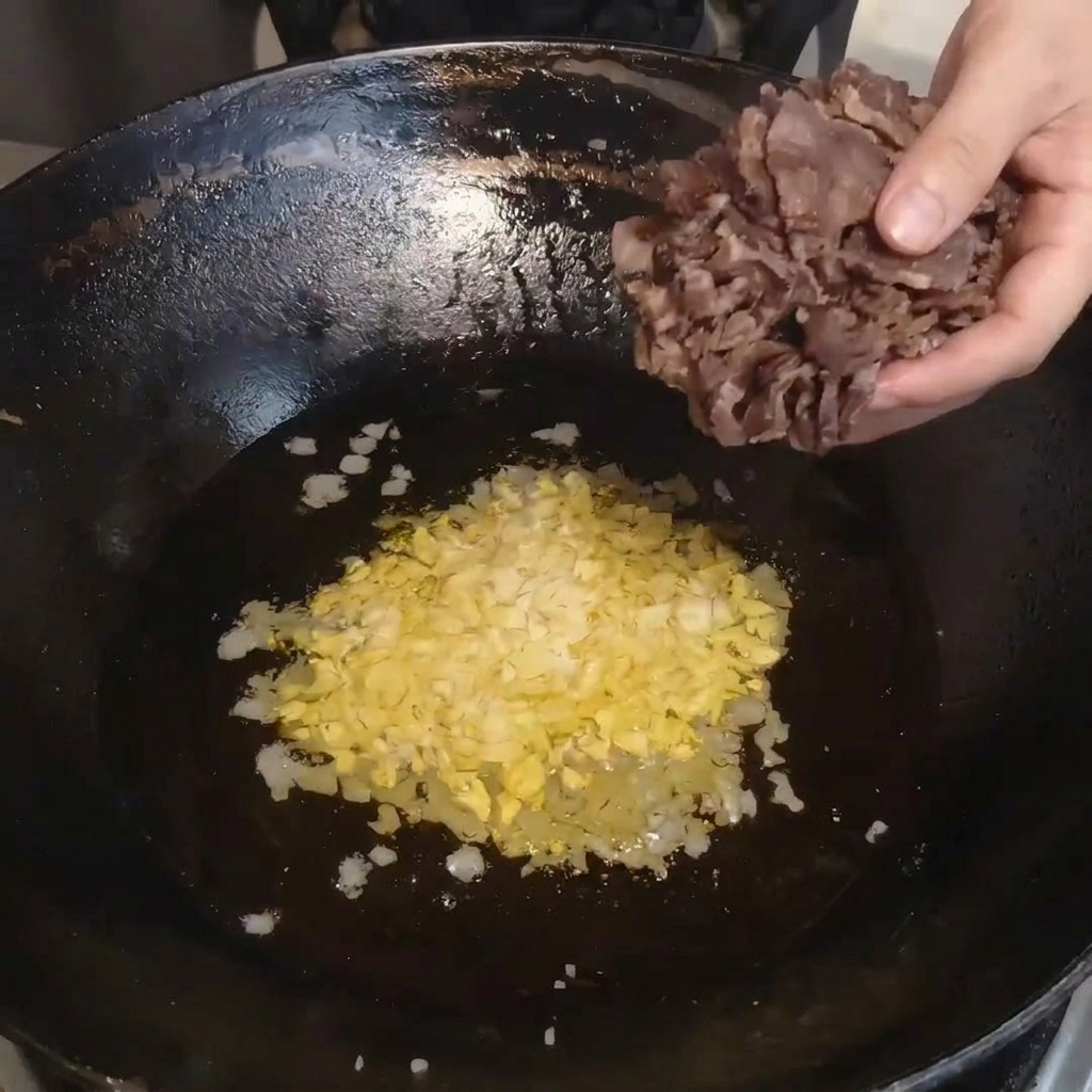 Steamed slices of cured beef being transferred from a bowl into a hot wok.