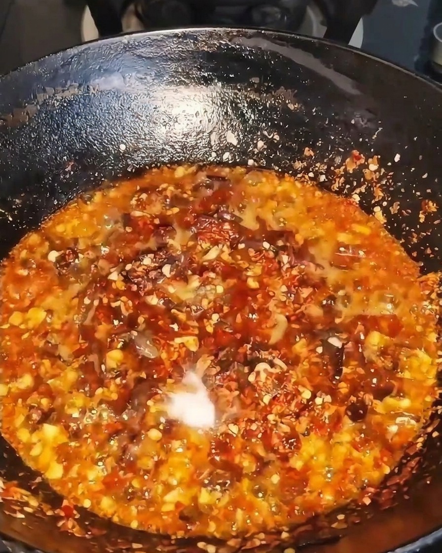 Dark liquid seasoning being poured into a sizzling wok filled with beef, chili, and aromatics.