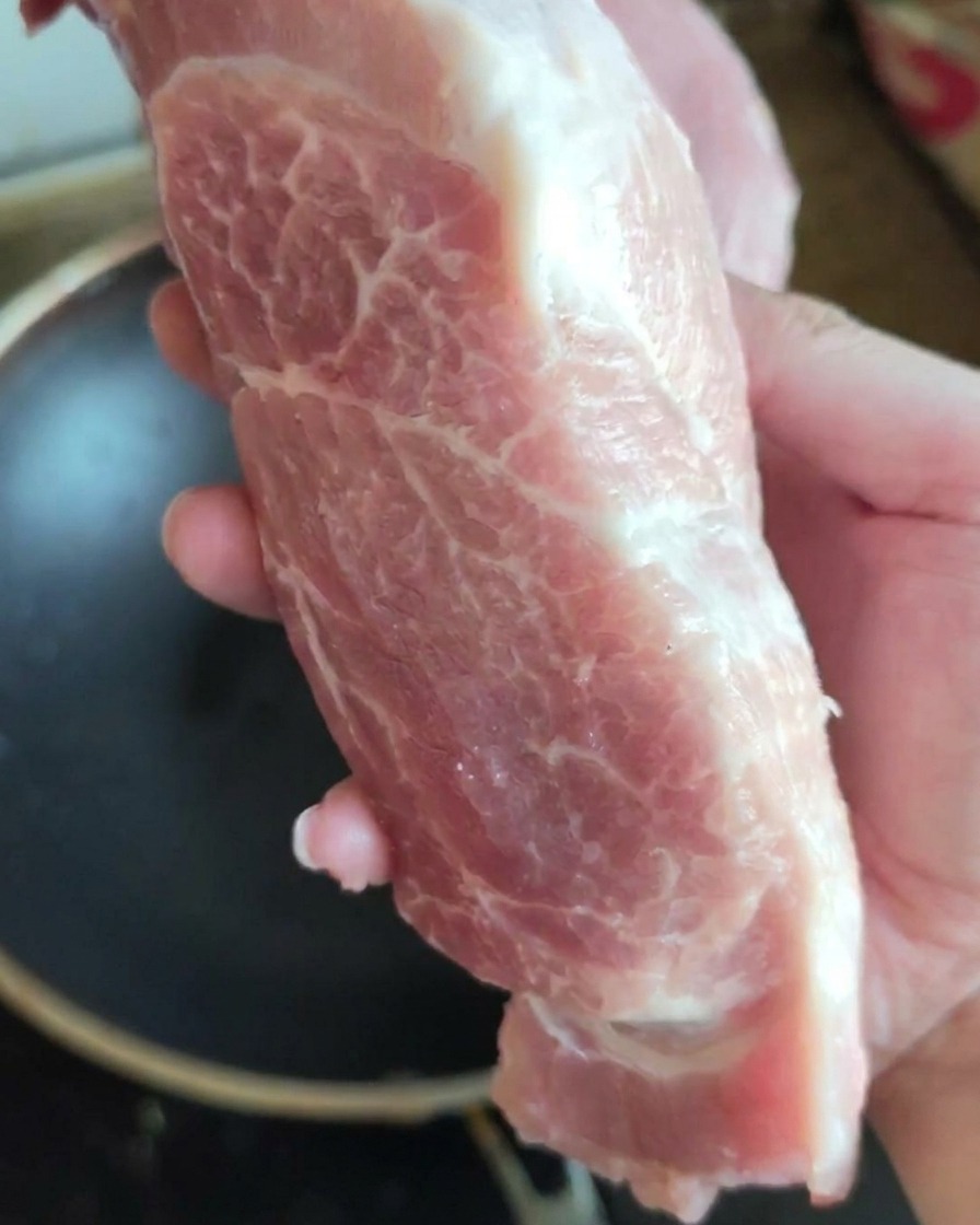 A large, fresh piece of raw pork shoulder being held up to the camera.