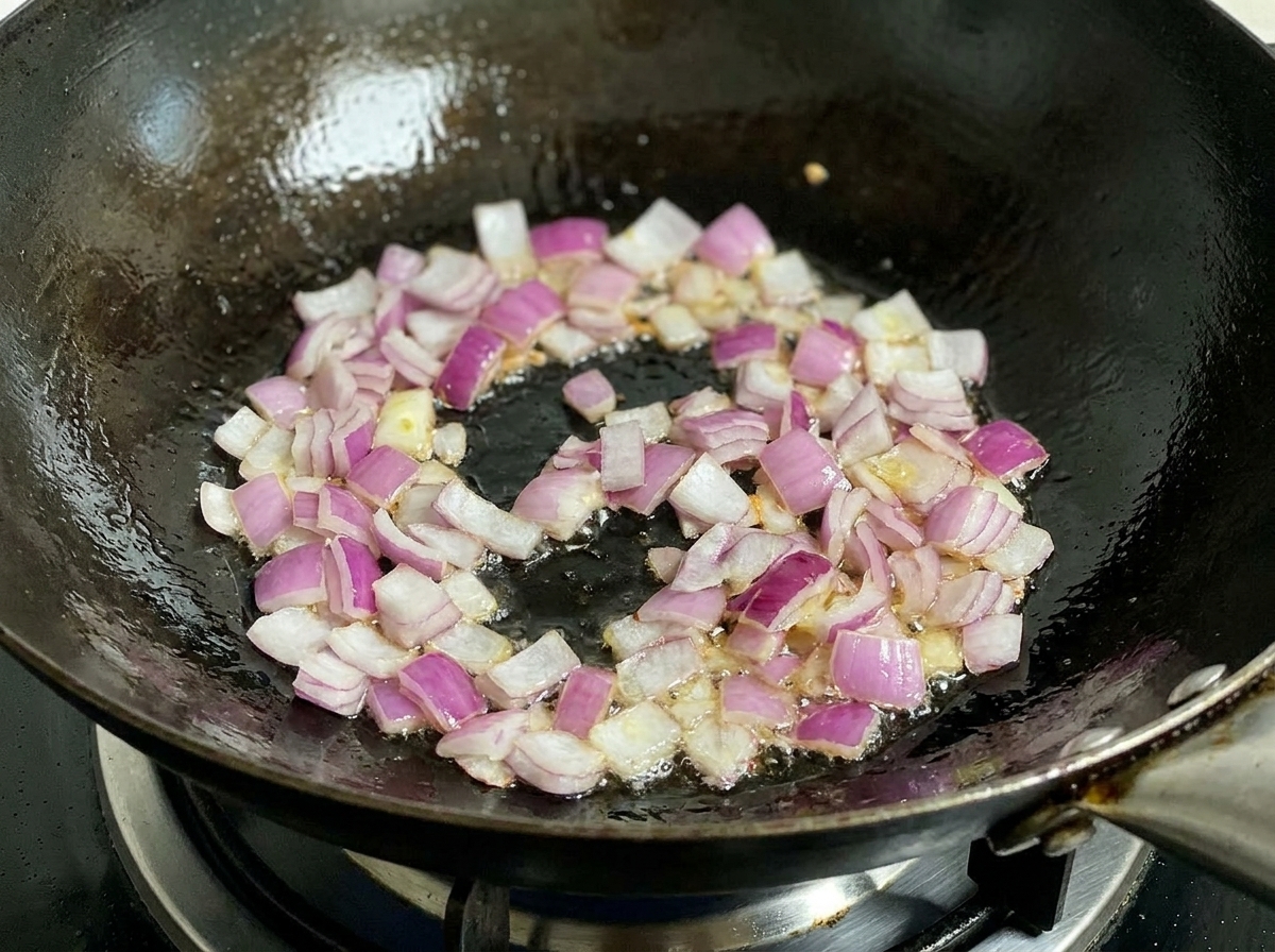 Chopped red onions frying in a hot wok with oil, being stirred by a black spatula.