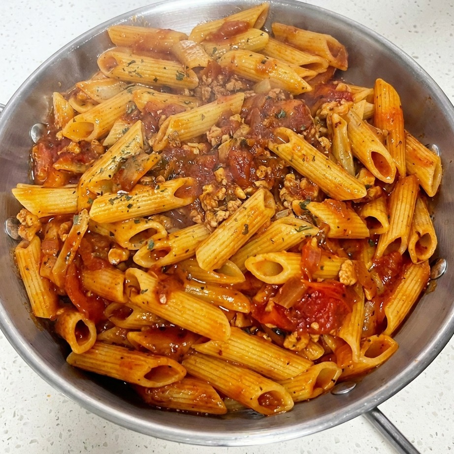 A close-up of a pan of tomato meat sauce macaroni topped with a single slice of cheese and freshly sprinkled dried green herbs.