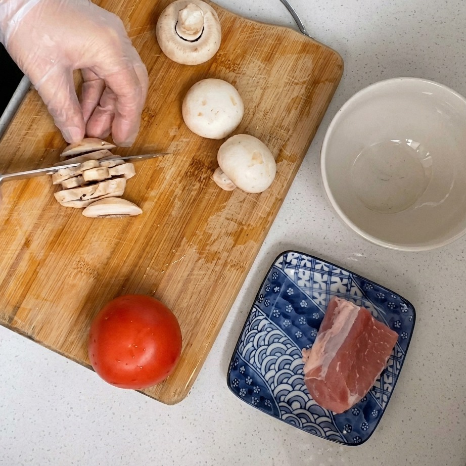 Fresh white button mushrooms being sliced into thin pieces on a wooden surface.