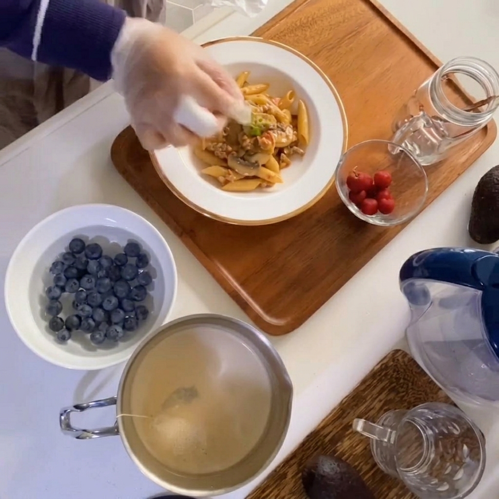 A close-up view of a hand placing a sprig of fresh thyme onto a bowl of creamy mushroom and meat macaroni.