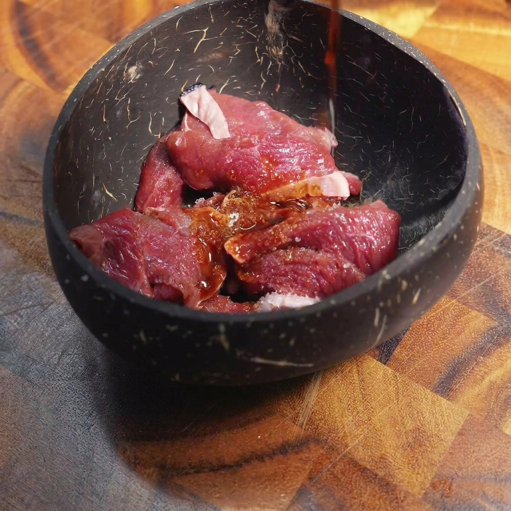 Dark marinade sauce being poured over raw, thinly sliced beef inside a dark bowl.