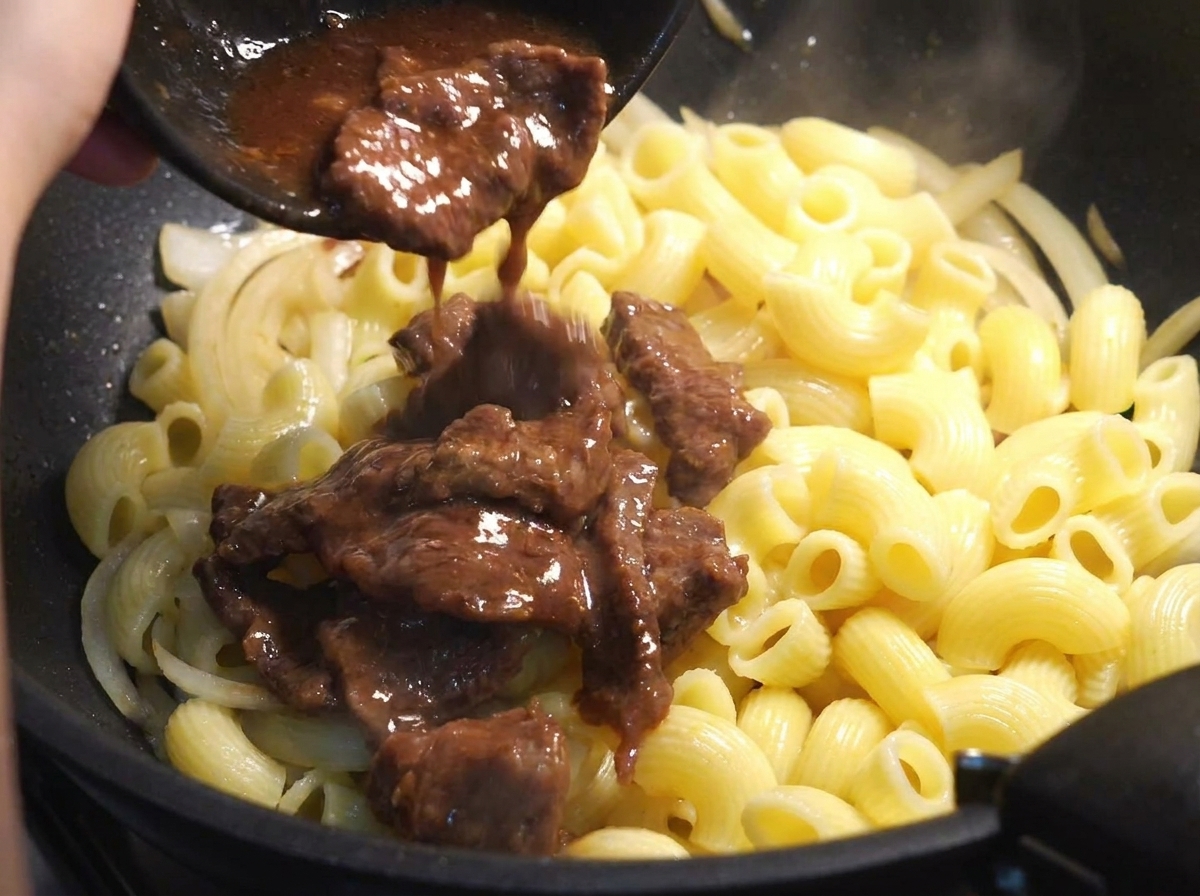 Partially cooked beef slices with marinade being added into a pan with macaroni and onions.