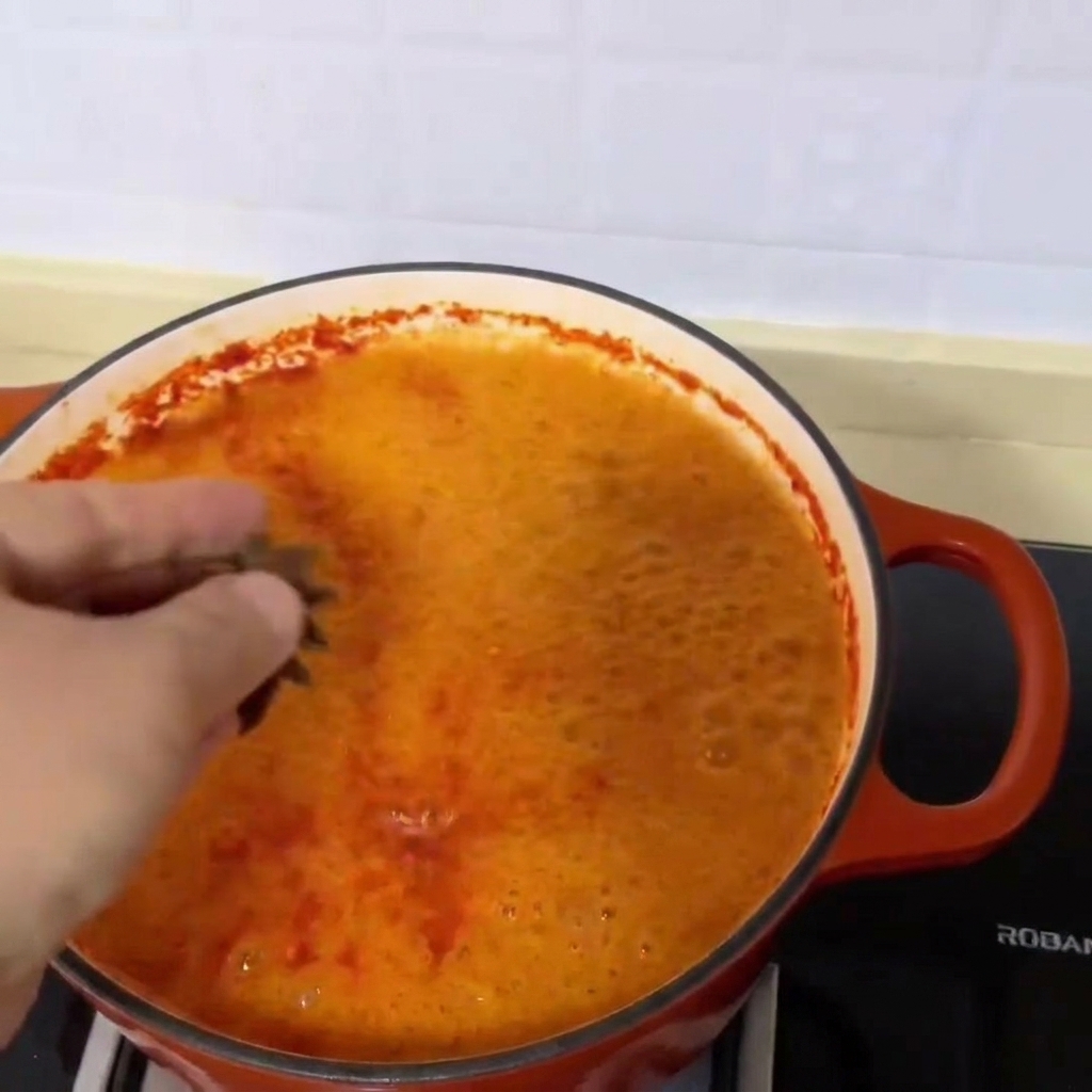Three star anise pods being dropped into the vibrant red, simmering clam soup.