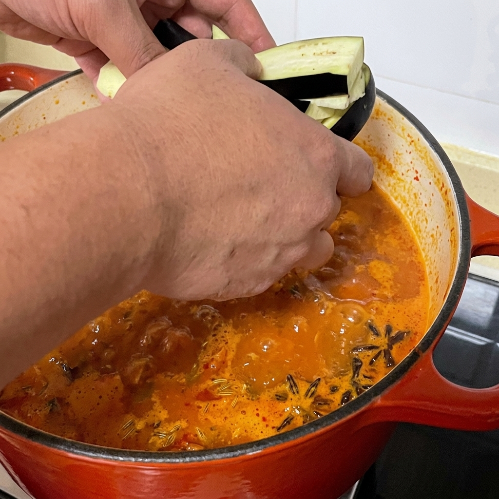 Sliced eggplant strips being added to the pot of spicy clam soup.