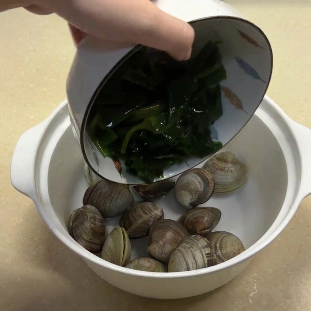 Rehydrated seaweed and ginger strips being added to the bowl of clams.