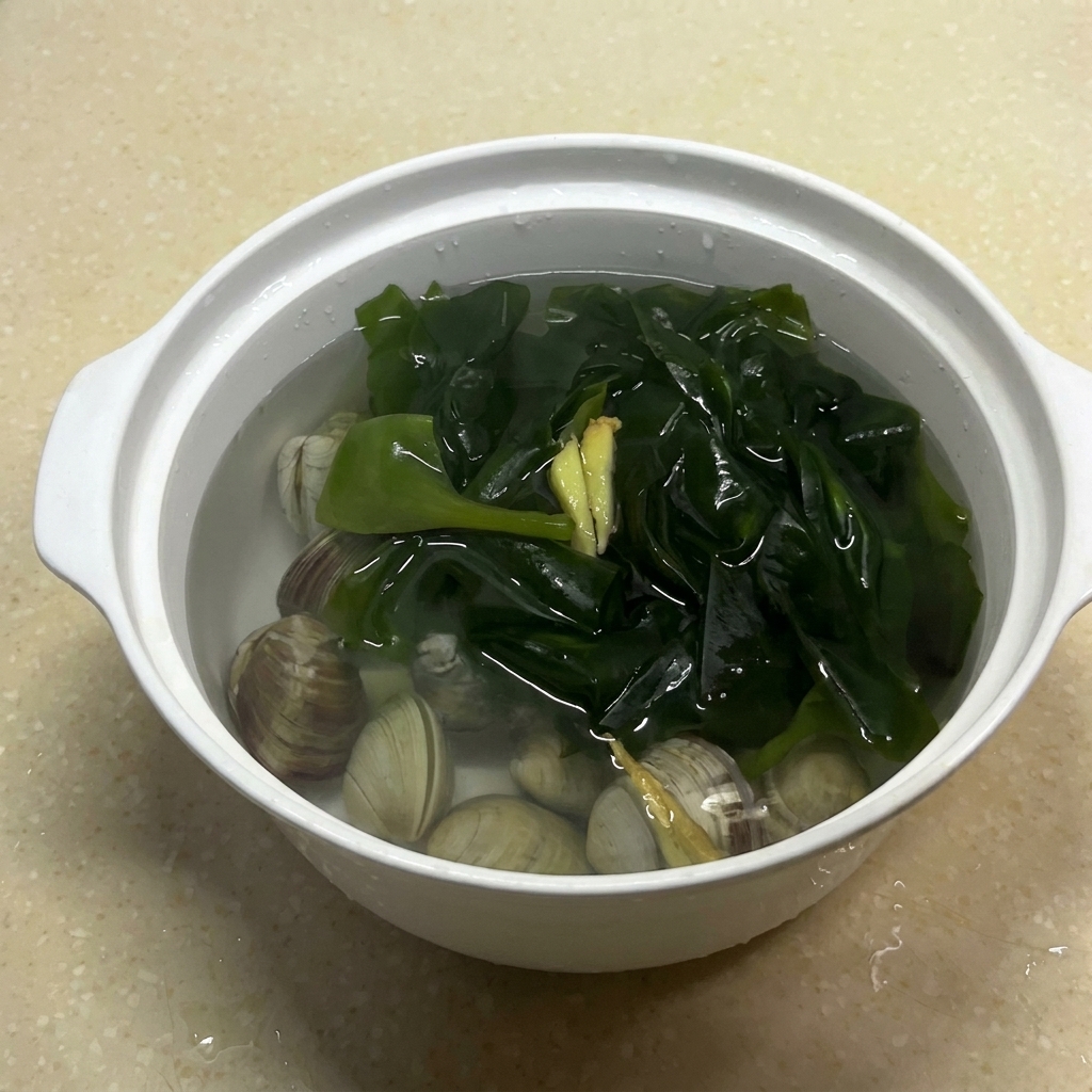 The bowl containing clams, seaweed, ginger, and water after adding salt.