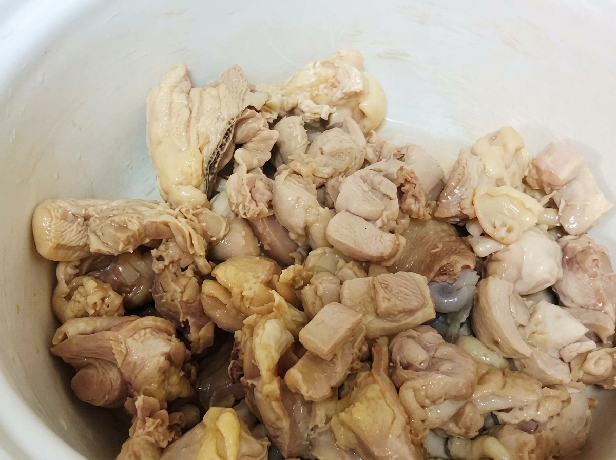 Blanched chicken pieces resting inside a white ceramic pot.