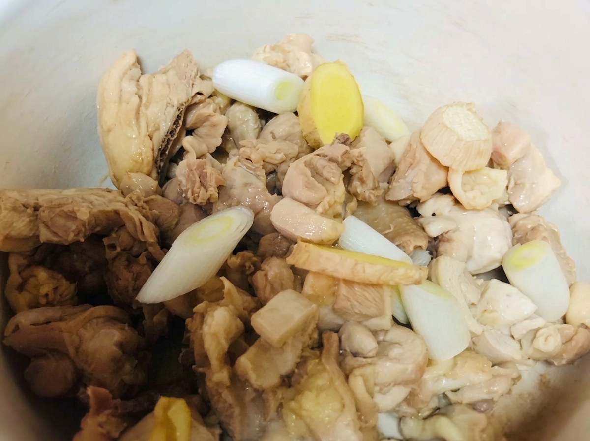 Chicken pieces in a clay pot seasoned with green onions, ginger, and liquid seasonings.