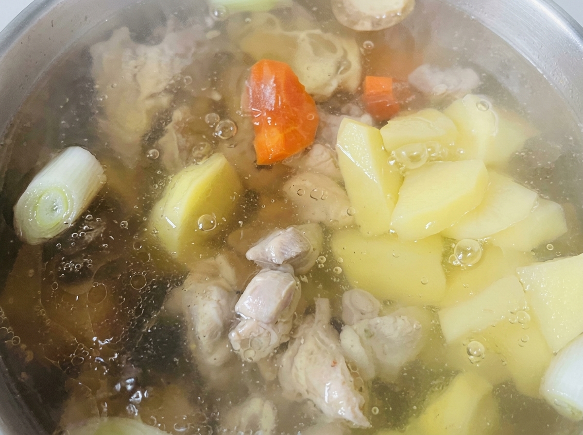 Chunks of carrots and potatoes cooking in a clear broth alongside the chicken pieces.
