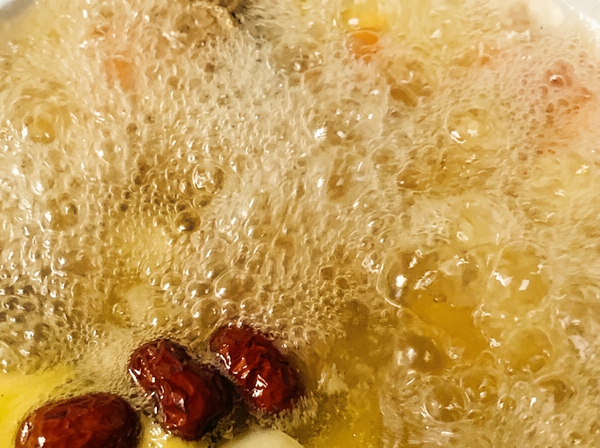 Red dates and seasonings being added to a pot of bubbling chicken soup.