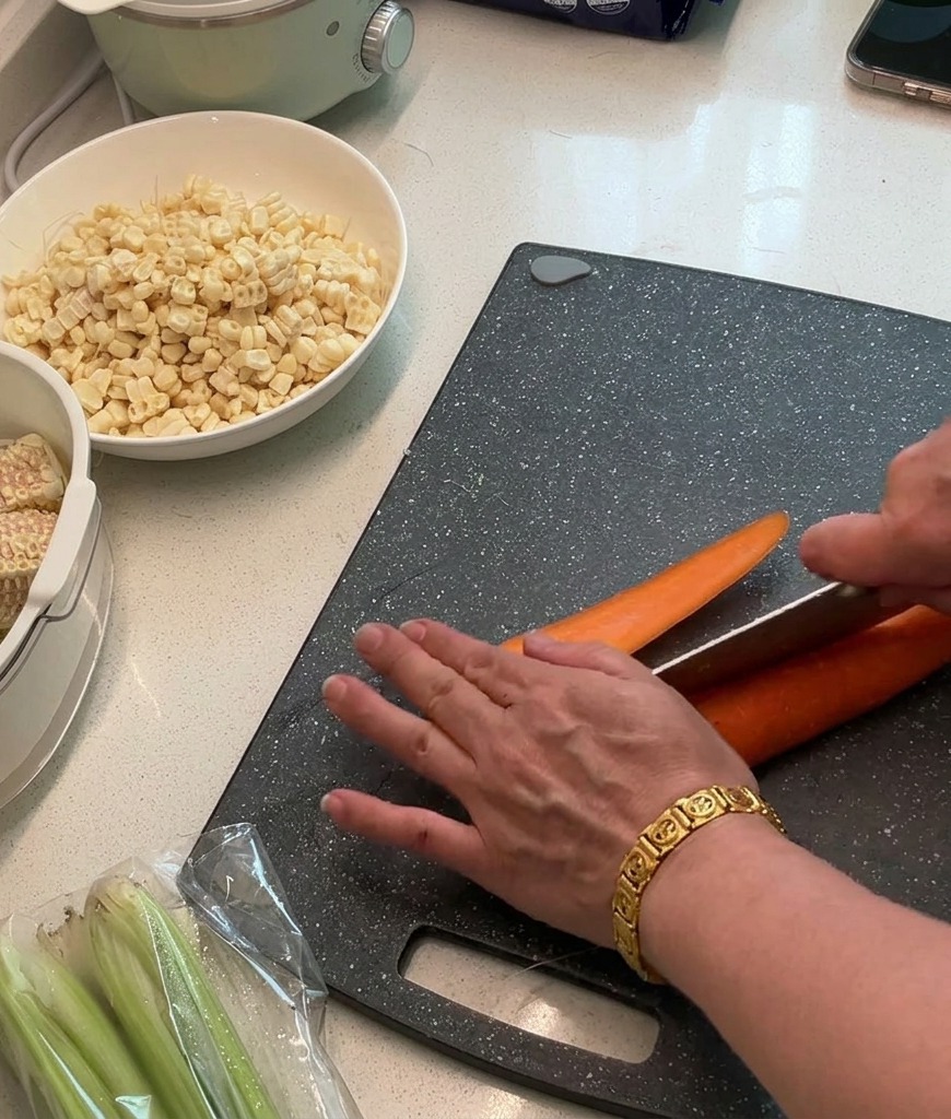 Fresh carrots being chopped into small, even dice on a dark cutting board.