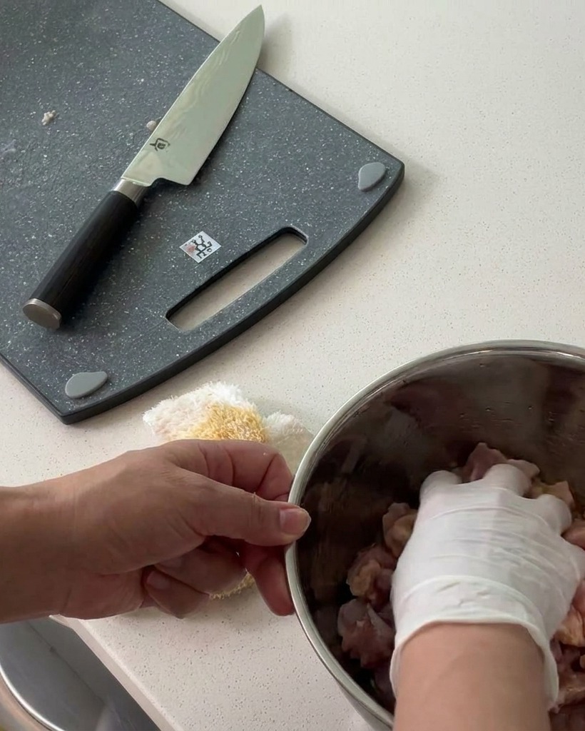 Diced chicken being tossed with seasonings in a metal mixing bowl.